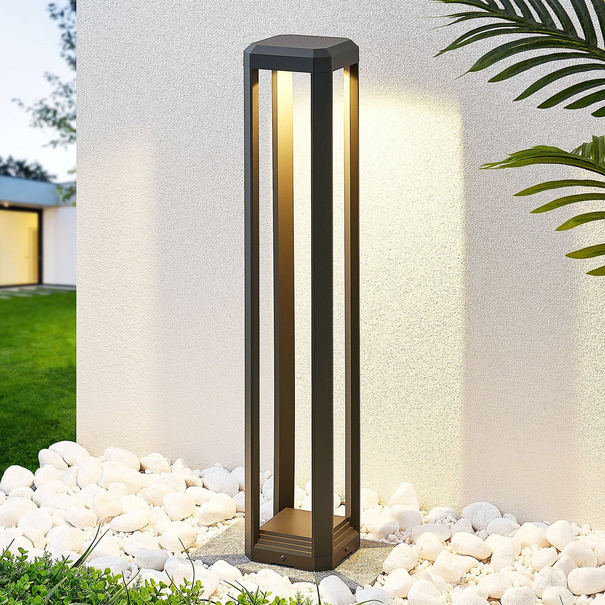 Feryn path light lit at dusk beside a rendered wall and a bed of white pebbles