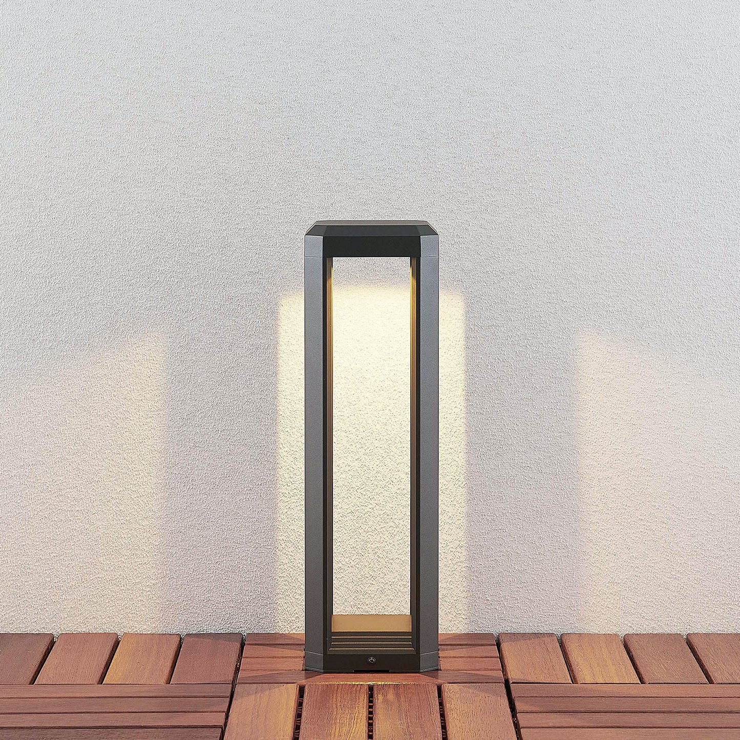 Ryda 50 cm bollard light on timber decking casting a warm downward glow onto a pale wall