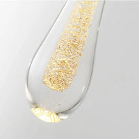 Macro detail of the crystal teardrop on the Golvara pendant, with gold flecks suspended inside the glass