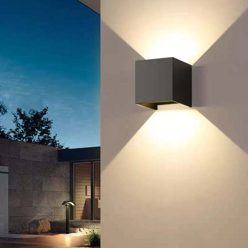 Nexo black cube wall light glowing warm white on an exterior wall at dusk