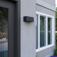 Bexa outdoor wall light mounted in daylight beside a front door, showing the flat anthracite housing against pale render