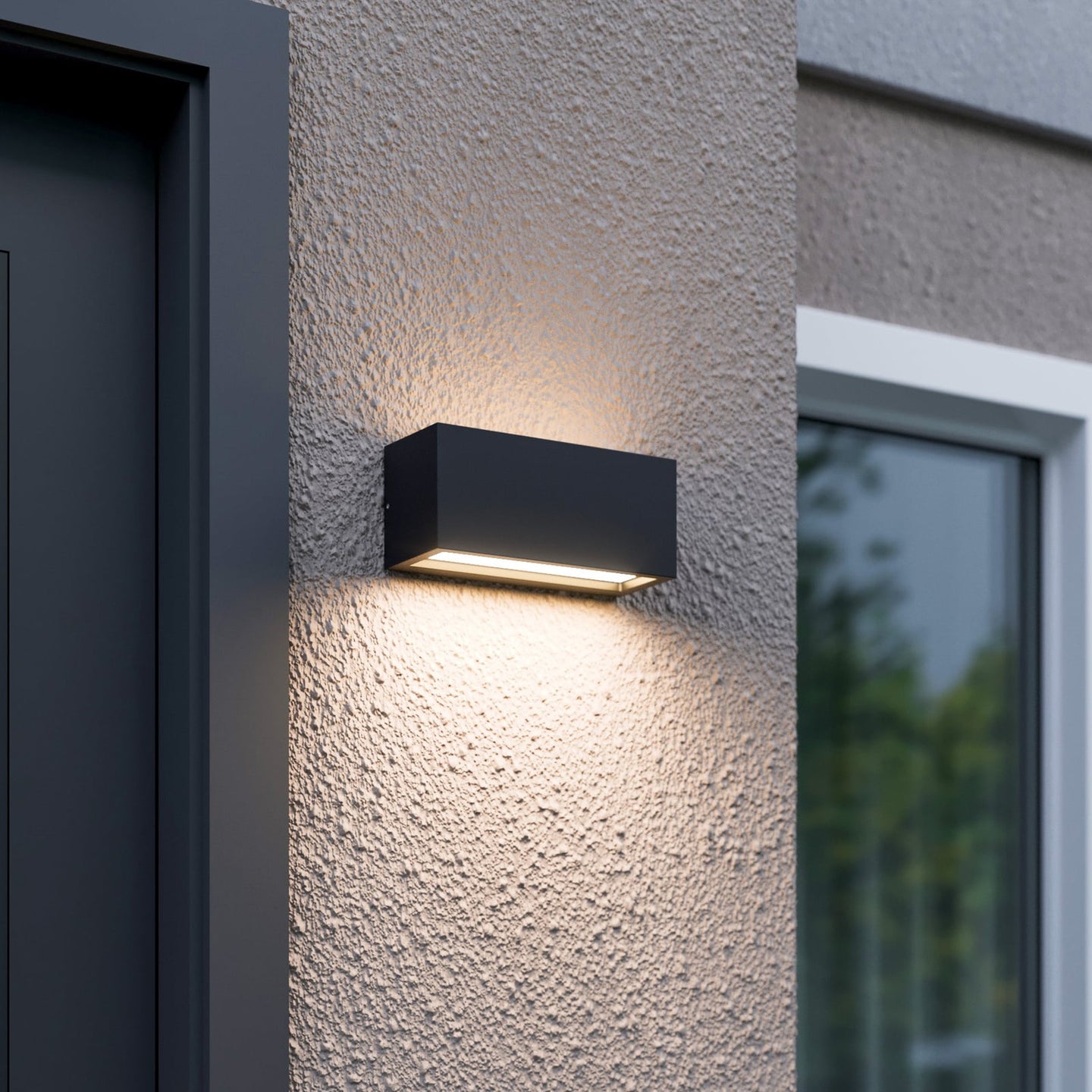 Bexa outdoor wall light lit beside a front door, casting a warm beam up the render and a wider pool of light down the wall