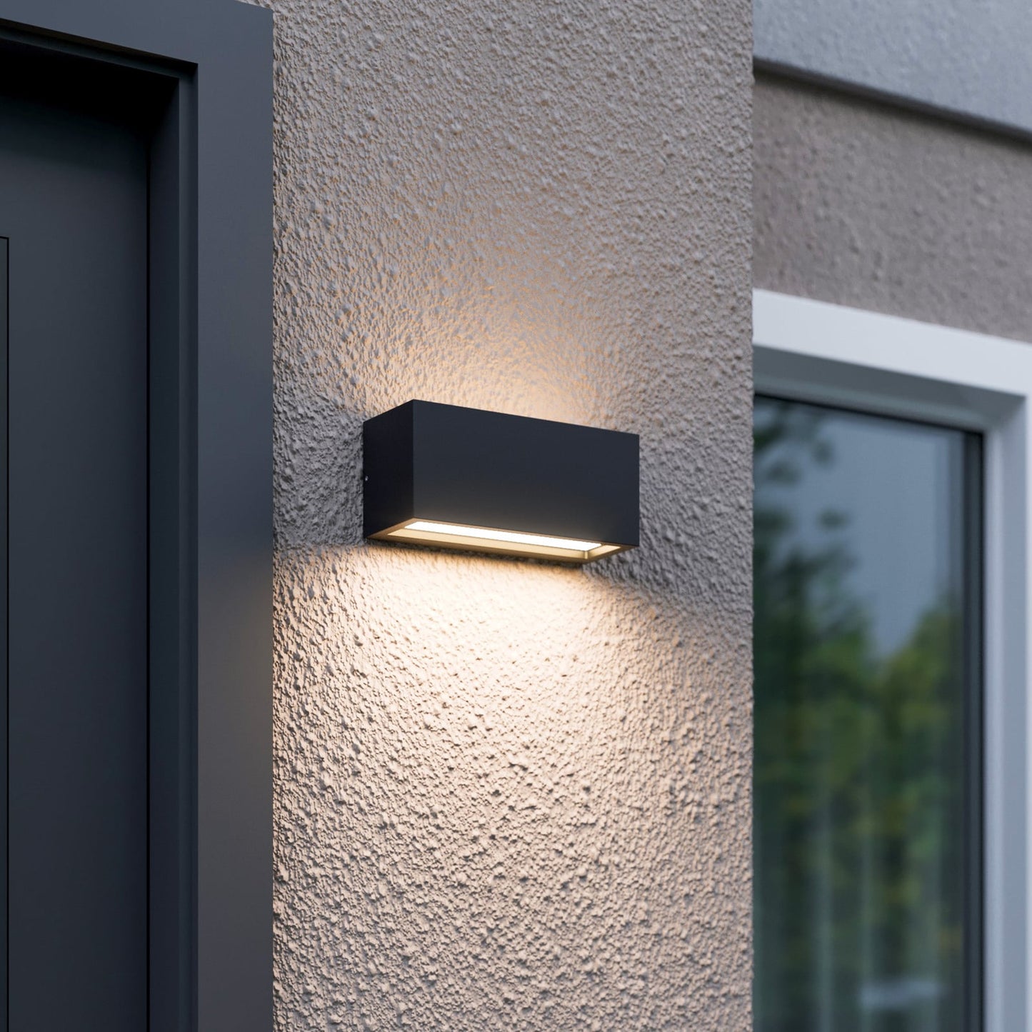 Bexa outdoor wall light lit beside a front door, casting a warm beam up the render and a wider pool of light down the wall