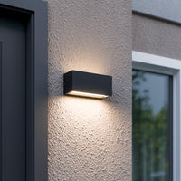 Bexa outdoor wall light lit beside a front door, casting a warm beam up the render and a wider pool of light down the wall