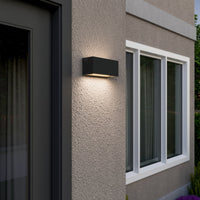 Bexa outdoor wall light switched on at dusk on a house corner beside a window, showing the twin up and down light spread
