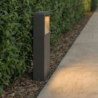 Leyo Pedestal Path Light glowing warm white beside a garden hedge at dusk