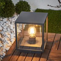 Anle Glass Pillar Light lit on a timber deck beside white pebbles and clipped box