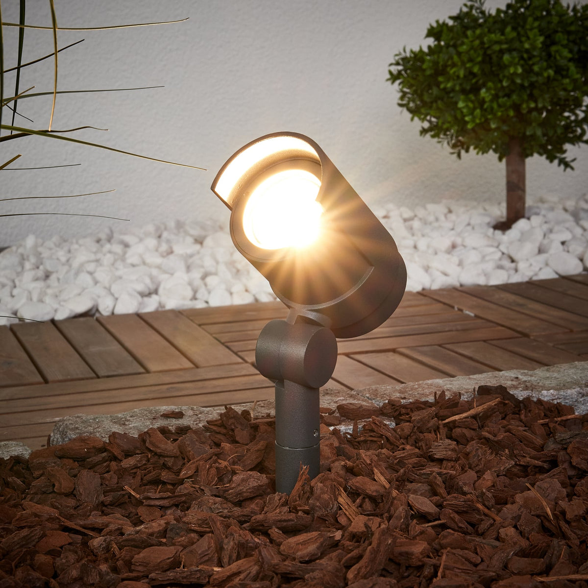 Batra Garden Spike Light glowing warm white in a garden bed at night