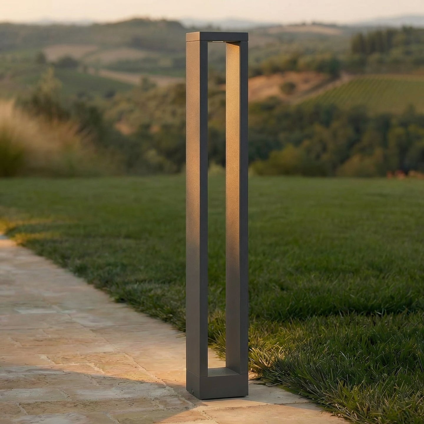 Jupo path post light lit at dusk beside a stone garden path, warm downward glow on the paving