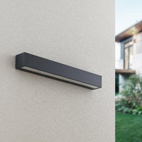 Lino Column outdoor wall light unlit in daylight on a rendered house wall, showing the anthracite finish and slim horizontal profile