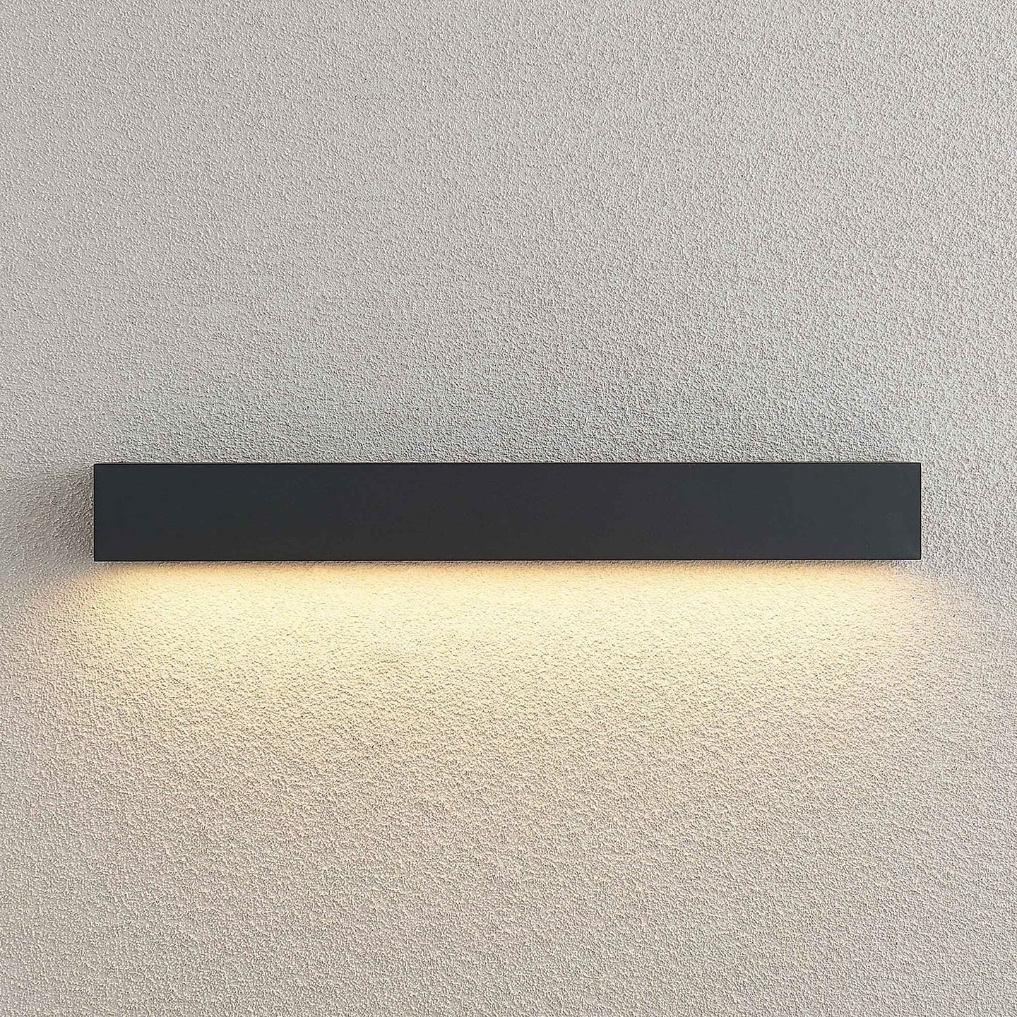 Close view of the Lino Column outdoor wall light lit against a textured render wall, showing the even downward wash of warm light