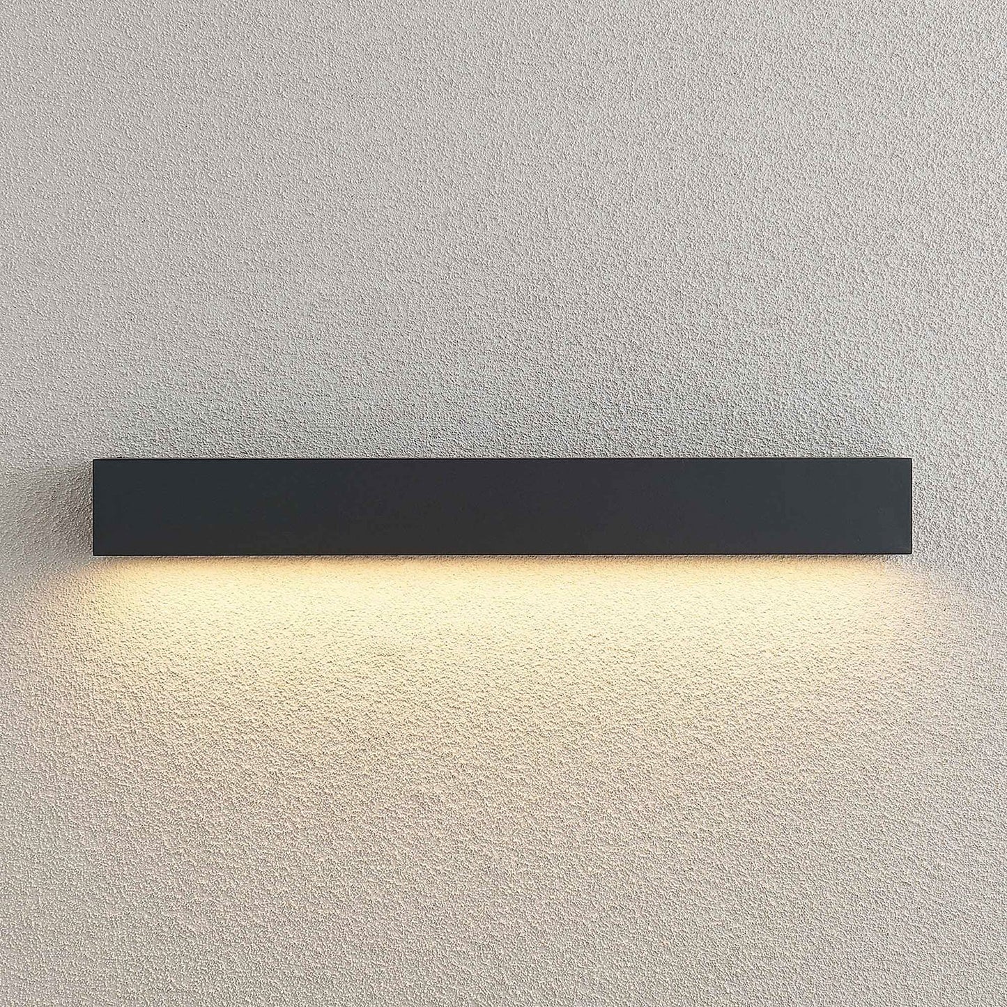 Close view of the Lino Column outdoor wall light lit against a textured render wall, showing the even downward wash of warm light