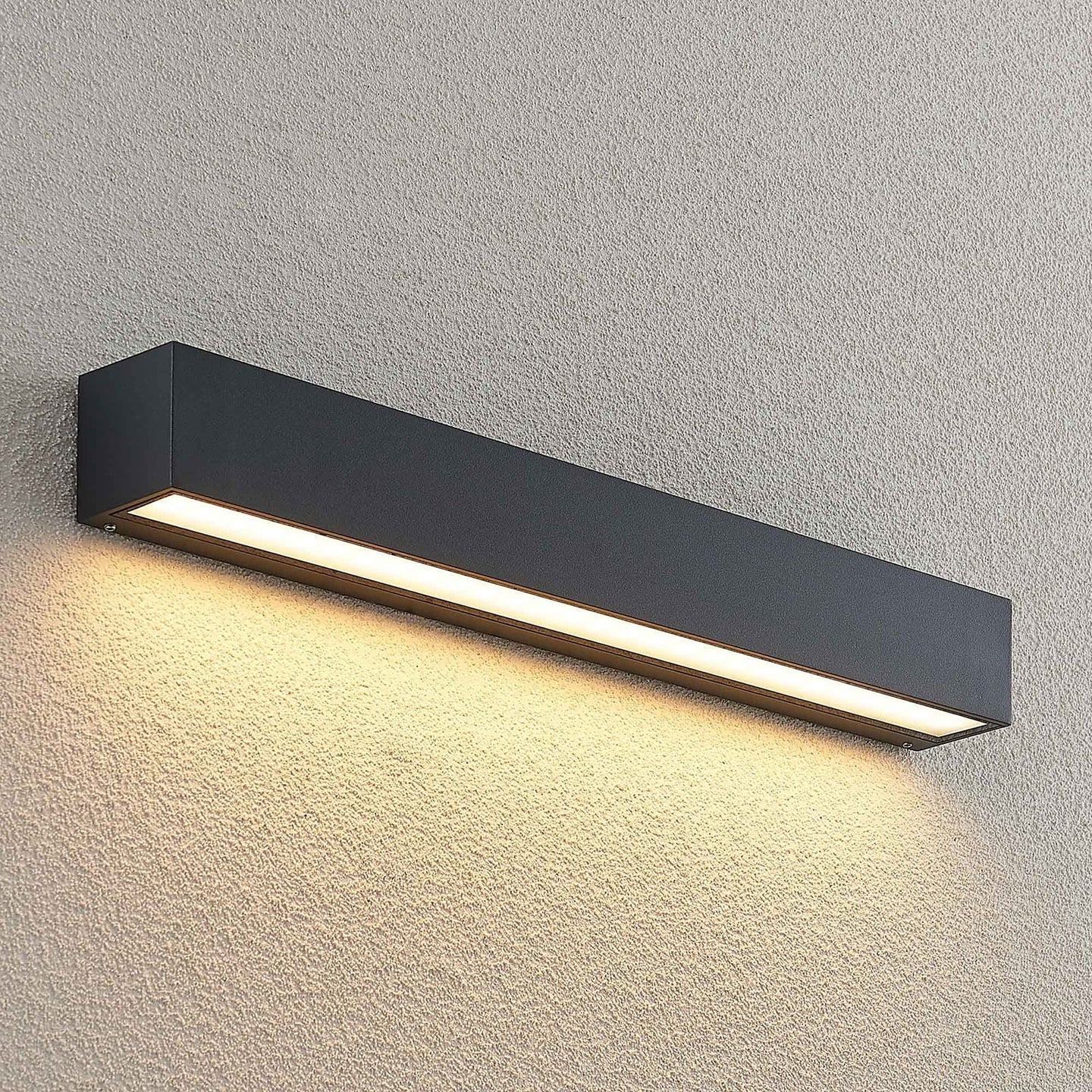 Lino Column outdoor wall light mounted on a pale rendered exterior wall and lit, seen from a wider angle