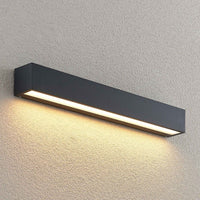 Lino Column outdoor wall light mounted on a pale rendered exterior wall and lit, seen from a wider angle