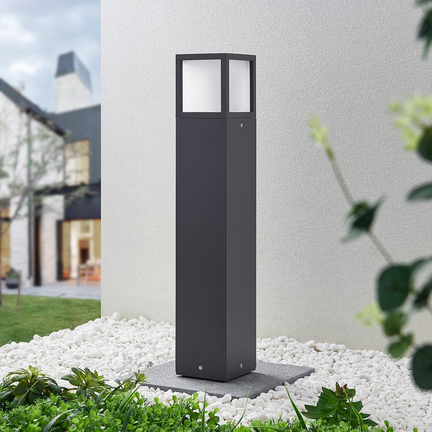 Dewa path post light installed in a garden at dusk beside white pebbles and planting