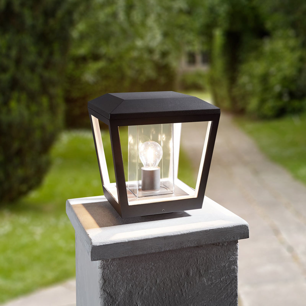 Dunara pillar light glowing on a garden wall post beside a hedge and driveway