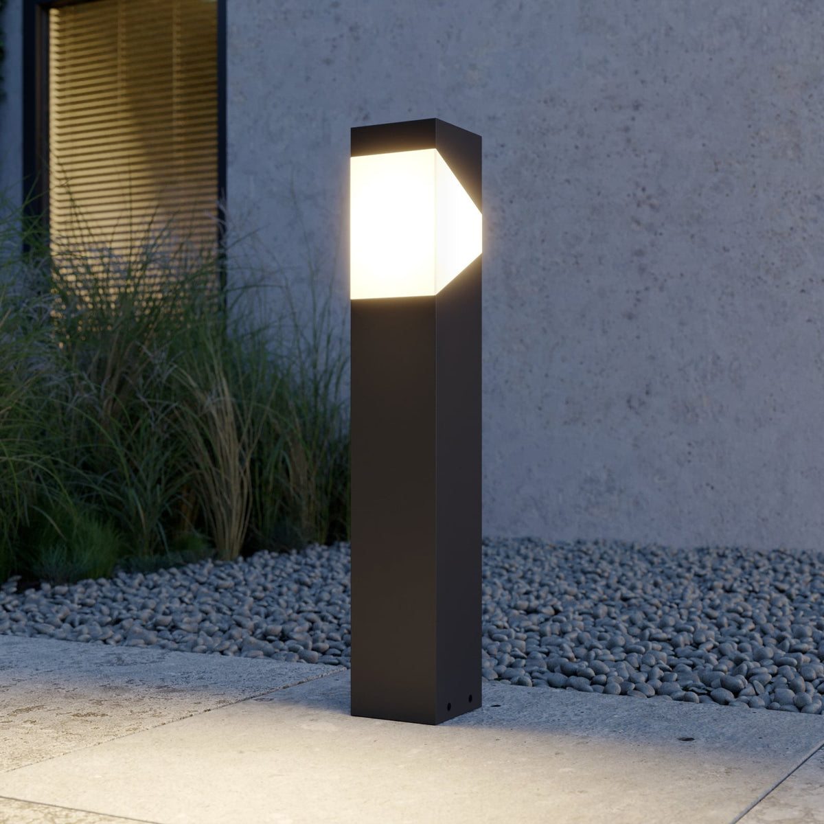Kiro Pillar Post Light glowing warm white beside ornamental grasses at dusk