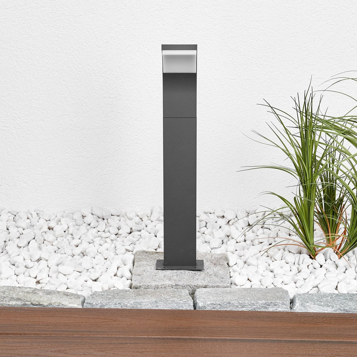 Wider garden view of the Timo anthracite path post light set into a gravel border beside a paved edge