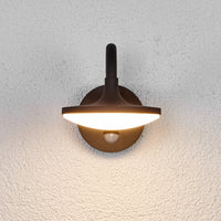 Front view of the Finno wall light lit, showing the disc shade and sensor lens on the mount