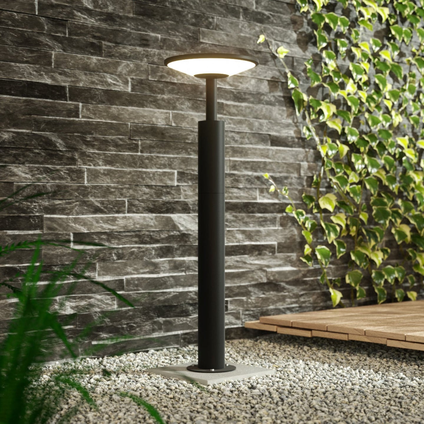Feno post light illuminated on gravel against a dark stone wall with climbing ivy