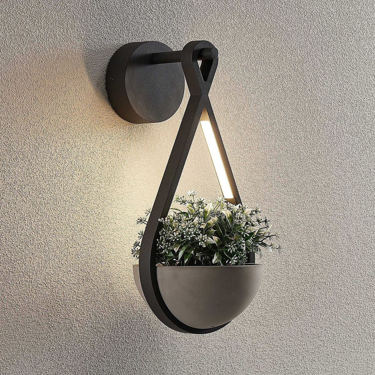 Norva Stone Planter Outdoor Wall Light lit at dusk with planting in the concrete bowl