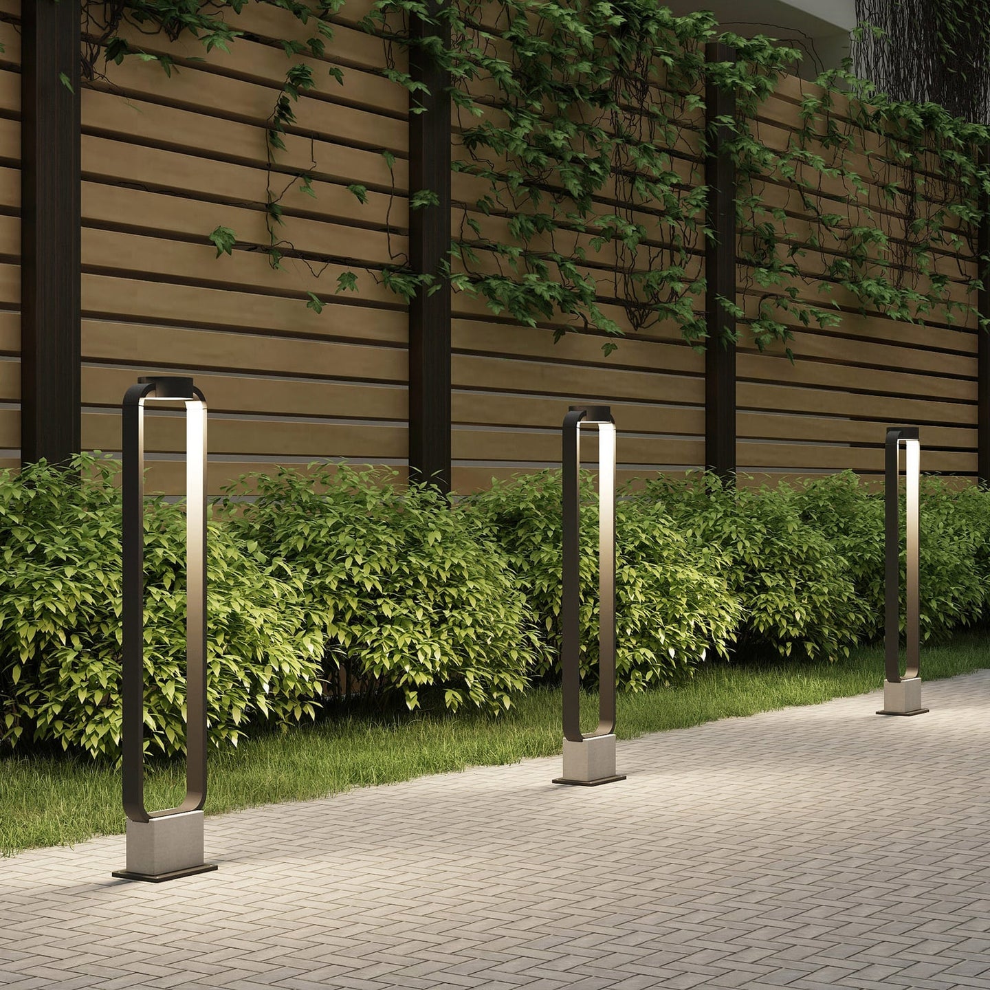 Three Talo bollard lights lit in a row along a paved garden path at dusk