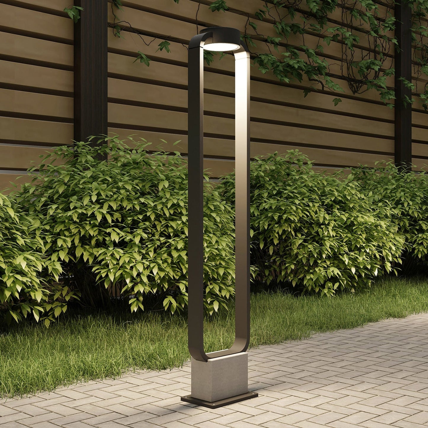 Talo bollard light lit beside a block paved garden path with hedging behind