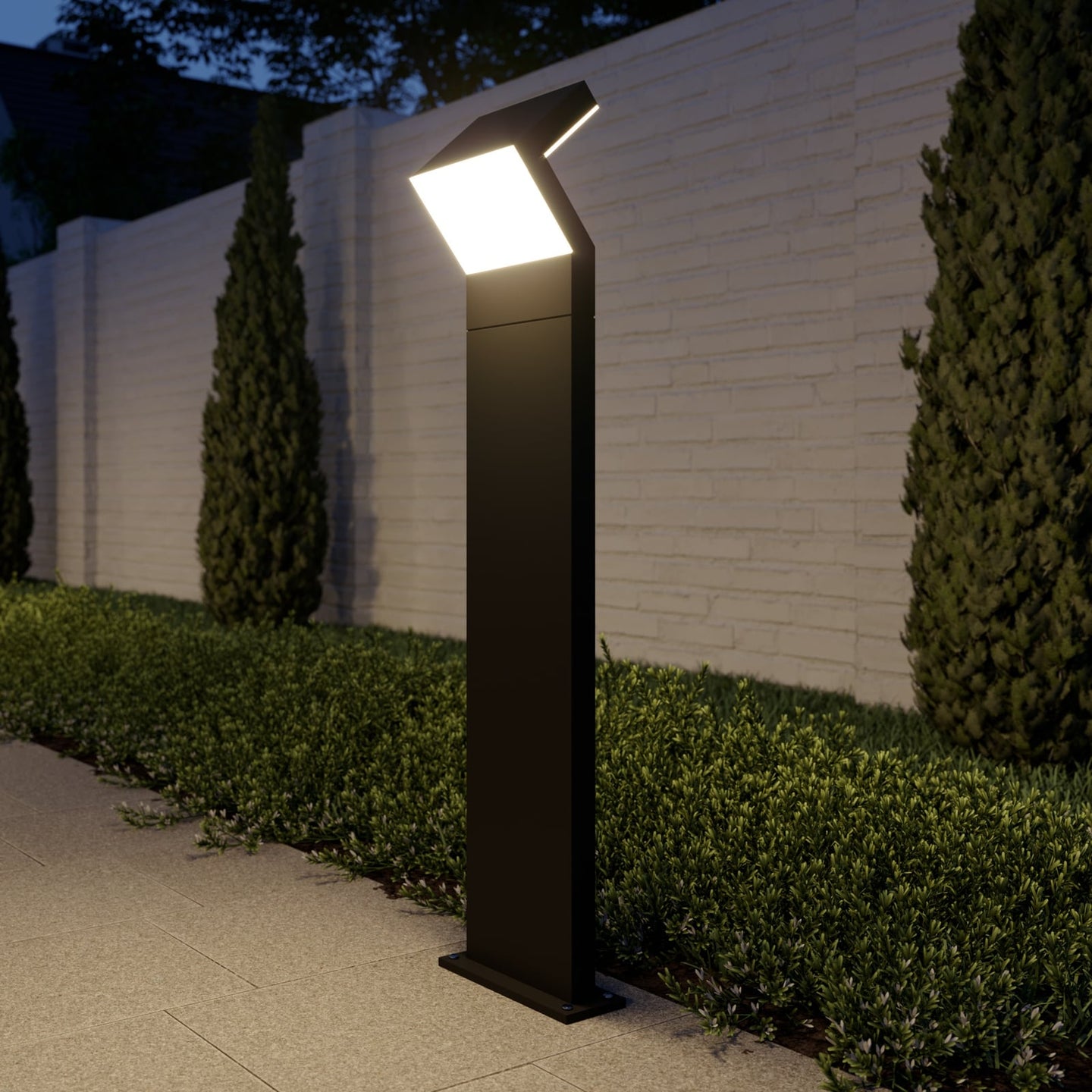 Havo Tall Path Light lit at dusk beside a clipped hedge and painted brick garden wall