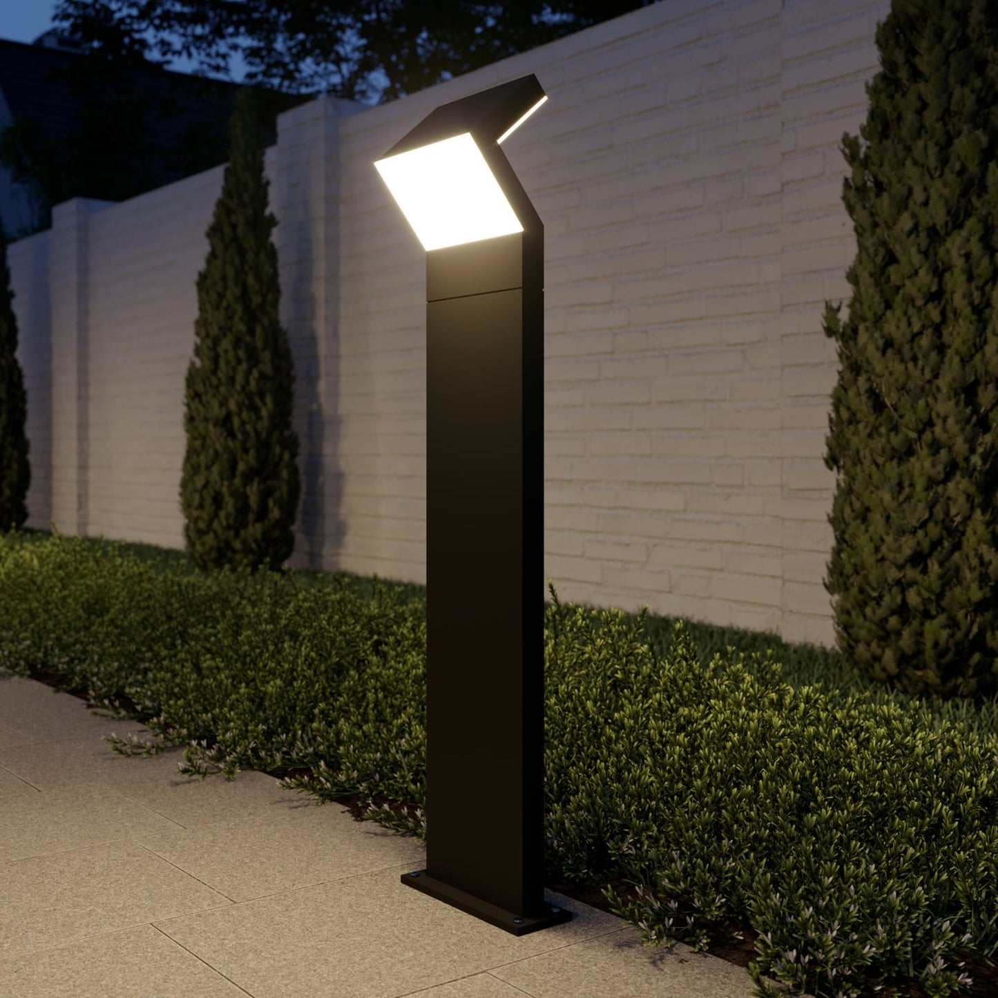 Havo Tall Path Light lit at dusk beside a clipped hedge and painted brick garden wall