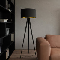 Beno tripod floor lamp beside a tan leather sofa and black bookshelf against a concrete wall