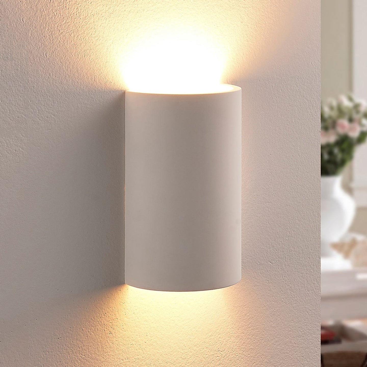 Cova wall light switched on, casting warm light up and down a pale plaster wall