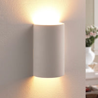 Cova wall light switched on, casting warm light up and down a pale plaster wall