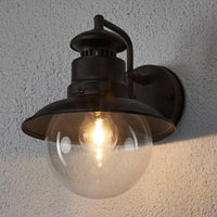 Erdo Rust Lantern Outdoor Wall Light lit on a rendered wall at dusk