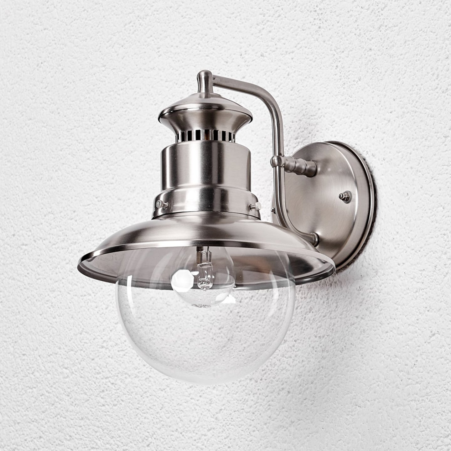 Gwena outdoor wall light mounted unlit on a white wall in daylight, showing the brushed stainless finish