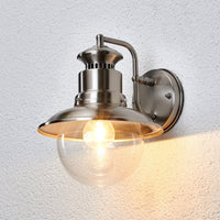 Gwena stainless steel outdoor wall light switched on against a white rendered wall, throwing warm light downwards