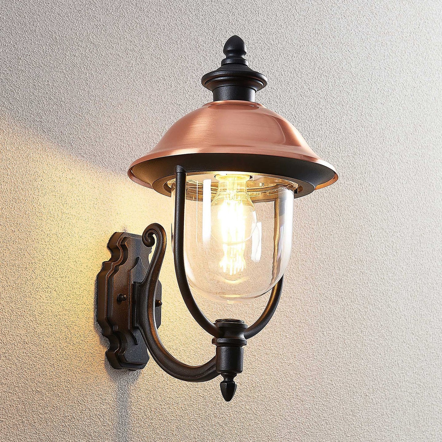 Koma copper wall lantern lit against a pale rendered exterior wall
