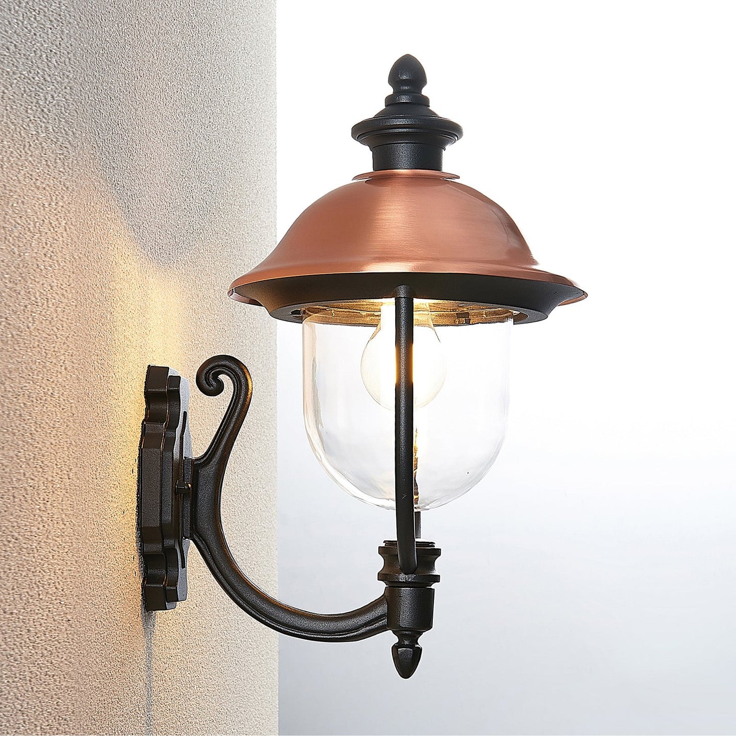 Koma copper lantern lit on an exterior wall corner showing the warm downward wash