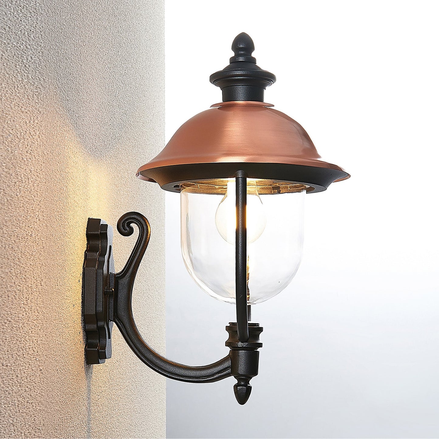 Koma copper lantern lit on an exterior wall corner showing the warm downward wash
