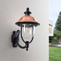 Koma wall lantern shown at an angle on a textured render wall with garden beyond