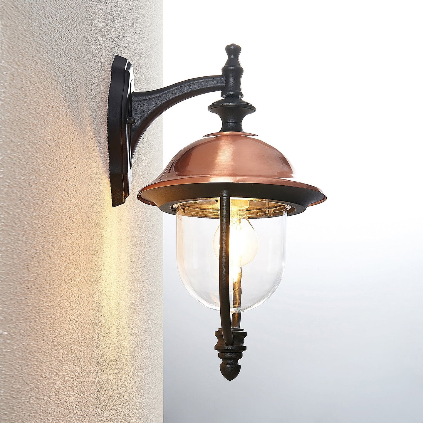 Side view of the Clivo copper outdoor wall light mounted on a wall corner, showing the curved black wall arm and copper roof