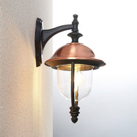 Side view of the Clivo copper outdoor wall light mounted on a wall corner, showing the curved black wall arm and copper roof