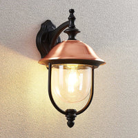 Clivo copper outdoor wall light switched on against a textured rendered wall, casting warm downward light