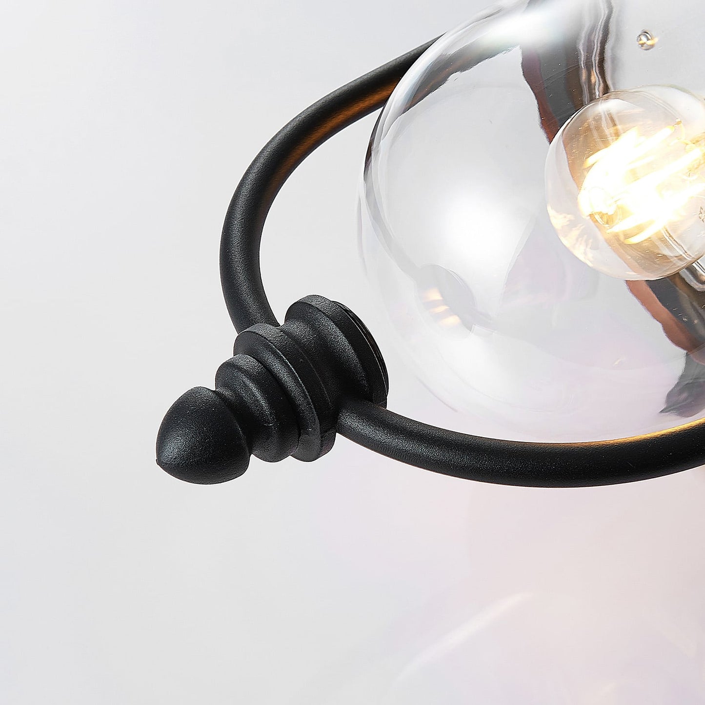 Detail of the Clivo outdoor wall light lower finial, black cage bar and clear diffuser with a lit filament bulb inside