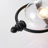 Detail of the Clivo outdoor wall light lower finial, black cage bar and clear diffuser with a lit filament bulb inside
