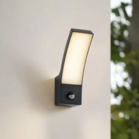 Close view of the Ilvo sensor wall light lit warm white on a pale exterior wall with the motion sensor eye visible