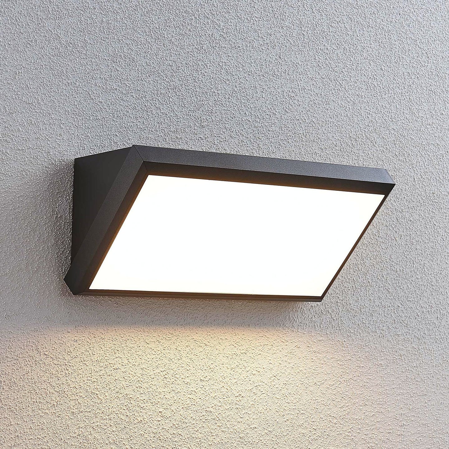 Abbo outdoor wall light lit on a textured grey wall casting a wide downward glow