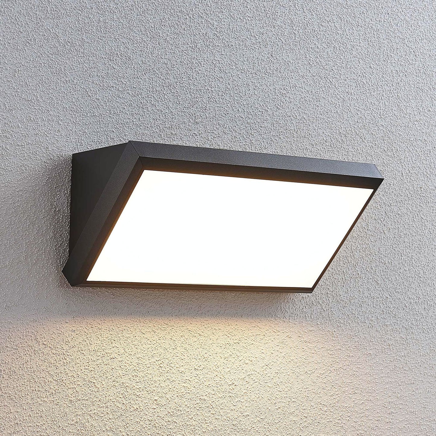Abbo outdoor wall light lit on a textured grey wall casting a wide downward glow