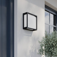 Auri square outdoor wall light in daylight on a white render wall, showing the dark grey cage frame and white glass face