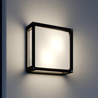 Auri square outdoor wall light switched on at night against a render wall, glowing evenly through the front and side glass panels