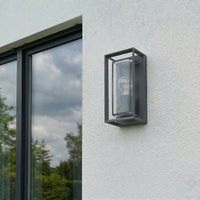 Isra lantern outdoor wall light unlit in daylight on a white house wall, showing the dark grey cage and clear glass against the render